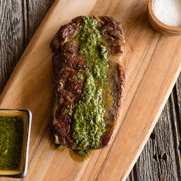 steak on a cutting board with pesto on top